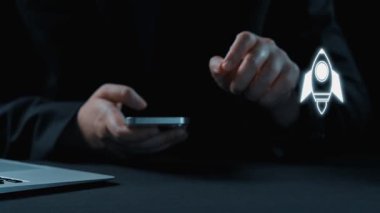 Bir insan akıllı telefon kullanırken, bir roket ikonu da iş büyümesini simgeliyor. Bu görüntü, yenilikçi ve girişimci ruhu modern bir çalışma alanında yakalar. Dörtgen