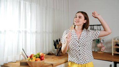 Enerjik beyaz anne kahvaltı için salata pişirirken ve yemek pişirirken elinde kepçeyle şarkı söylüyor. Sağlıklı yemek yapmaya hazırlanırken müziğe yönelen mutlu ev sahibi. Pedagoji.