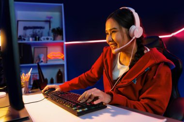 İnternet üzerinden kulaklık takıp gülümseyen Asyalı güzel kız flamasının sunucu kanalı izleyicilerle internet üzerinden konuşma yapıyor. Esport yetenekli takım oyuncuları neon mavi odada. Taktik.