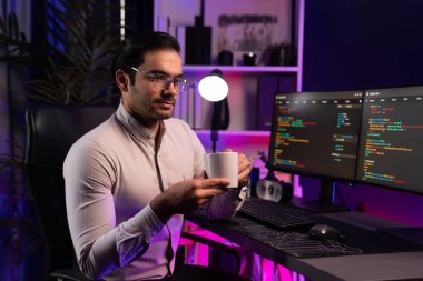 Akıllı IT geliştiricisi, bilgisayar ekranında yazılım geliştirme kodlu kahve fincanı tutuyor. Dışarıya bakıyor, program güncellemesi internet sitesi verilerini neon ışıklı siber ofiste sunuyor. Tahmin et..