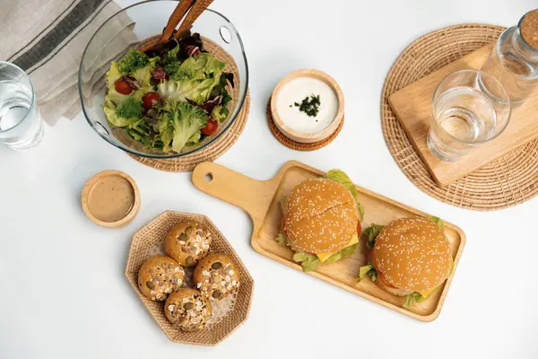 Çifte köfteli hamburger, salata, beyaz masa arkasında ev yapımı servis edilen yemeğin kepekli çöreği. Restoran ya da kafe menüleri hazırlanıyor. İnfobahn.