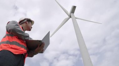 Gökyüzü arka planına sahip bir rüzgar türbini üzerinde çalışan mühendis. Yenilenebilir ve sürdürülebilir enerjinin gelecekteki üretimi için yenilikçi bir ideal. Rüzgar türbininden enerji üretimi.