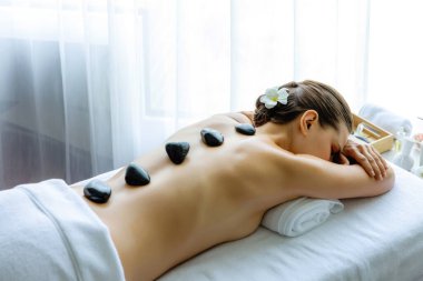 Lüks tatil köyündeki kaplıcalarda sıcak taş masajı. Gün ışığı sükunet ortamında, mutlu kadın müşteri bazalt taş masajından zevk alıyor. Rahatlatıcı bir sıcaklıkla vücudun üzerinde süzülüyor. Sessiz.