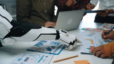 Veri analizinde yardımcı olan robotik bir kolu sergileyen modern bir iş toplantısı, işbirlikçi bir ortamda takım çalışması ve yeniliklerin altını çiziyor. Noogenesis