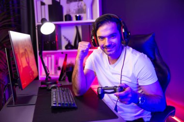 joystick oyuncusuyla akıllı oyun flaşçısı kameraya bakıyor, savaş takımının arka planında savaş gemisine ateş ediyor yan görüntüde, dijital neon ışık stüdyosunda kulaklık takıyor. Tahmin et..