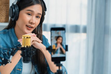 Asyalı sunucu canlı yayında canlı yayında canlı yayında sosyal medyada kulaklık takarak konuşuyor. Dinleyicileri modern stüdyoda koçluk yaparak selamlıyor. Taktik.