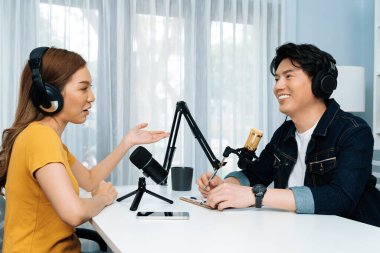 Gülümseyen radyo etkili sunucusu kulaklık takıyor kadın konuşmacı ile röportaj yapıyor sosyal medya internet sitesinden dinleyicilere bilgi paylaşıyor stüdyo kaydında sabah canlı yayın kanalı. İnfobahn.