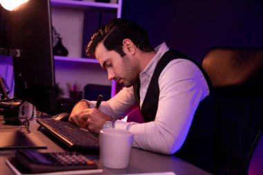 Stresli akıllı işadamı, kağıt işleri üzerine not pazarı verileri yazarak, gece geç saatlerde mor neon karanlık aydınlatma odasındaki disiplin ürünü hizmetlerinin çevrimiçi satış kanalını analiz ediyor. Tahmin et..