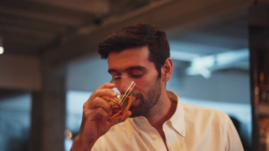 Profilde, beyaz tişörtlü, gülümseyen zeki bir adamın cuma gecesi lüks bir barda özel parti içeceği kokteylinden kokteyl içtiği görülüyor. Vinosity.