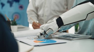 Robotik bir el, modern bir ofiste iş raporları ve grafikleriyle etkileşime geçerek, teknolojilerin takım çalışmasındaki rolünü ve üretkenliği artırmak için proje analizini vurgular.