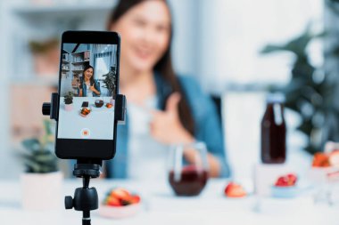 Seçici odaklı akıllı telefon ve gülümseyen genç, güzel Asyalı karışık çilek ve kiraz suyu detoksu değerlendirmesi sosyal medyada sağlıklı ürün tanıtımı sunuyor. Taktik.