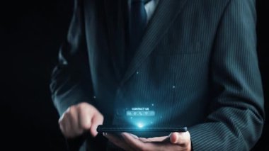 Bir işadamı, modern bir kurumsal ortamda çeşitli iletişim yöntemlerini temsil eden dijital temas simgelerini gösteren bir akıllı telefon tutuyor. Dörtgen