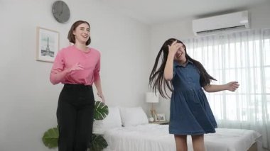 Yatak odasında Asyalı kızıyla müzik eşliğinde dans eden mutlu çekici anne. Beyaz anne dans eder ya da egzersiz yapar. Bu arada tatlı çocuk da müzik eşliğinde yatağa atlar. Aile eğlence konsepti. Pedagoji.