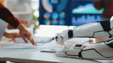 Modern bir ofiste insan ve robot kol arasında yaratıcı bir işbirliği. Olay yeri, yakın etkileşim yoluyla veri analizi ve yenilikçi takım çalışması stratejilerini vurguluyor. Noogenesis