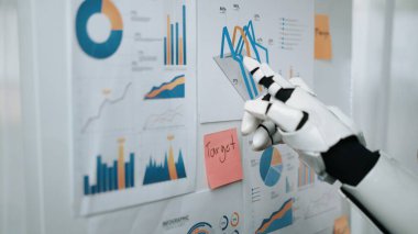 Bir robot kol, modern bir çalışma alanında veri analizi ve görselleştirmenin gösterildiği, duvarda gösterilen çeşitli grafik ve grafiklere işaret eder. Noogenesis