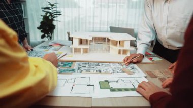 Mimarideki takım çalışmalarını ve yaratıcı tasarım süreçlerini vurgulayarak çağdaş bir ofiste plan ve çizimler üzerinde işbirliği yapan mimarları gösteren dinamik bir sahne. SACTR