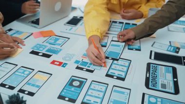 Hareketli bir beyin fırtınası, mobil uygulama tasarımı üzerinde çalışan çeşitli bir ekibi yakalıyor. Renkli maketler ve teknolojik aletler masaya yayılmış durumda. SACTR