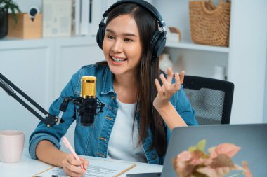 Sosyal medyada kulaklıkla canlı yayın yapan Asyalı sunucu modern stüdyoda yaşam koçluğu veya pazarlama dinleyicilerini selamlıyor. Taktik.