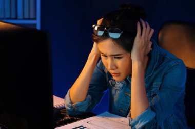 Stresli, genç, güzel Asyalı yaratıcı proje yaratıcısı sosyal medyayı araştırmak için bilgisayara bakıyor ve geceleri daha çok neon modern ofisin planlama kanalı stratejisine ulaşılıyor. Taktik.