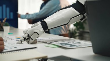 Modern bir ofisteki insan meslektaşlarıyla etkileşen robotik bir kolu vurgulayan çarpıcı bir sahne. Görüntü, teknoloji odaklı çalışma alanındaki takım çalışmasını ve yeniliği vurguluyor. Yaratıcılık