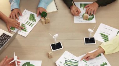 Eko evi projesini yel değirmeni tasarım modeli ve karbon ayak izini azaltmak için yeşil enerji kullanım grafiği ile toplantı masasında tartışan harika bir iş ekibi. Dünyayı kurtarın. Eline odaklan. Tanımlama.