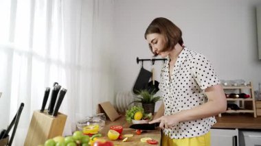 Enerjik anne, mutfak malzemeleri ile çevrili sebzeleri doğrarken modern mutfakta kahvaltı için salata yapıyor. Akıllı kadın temizlikçi yemek pişirir ve yemek hazırlar. Sağlıklı bir yaşam tarzı. Pedagoji.