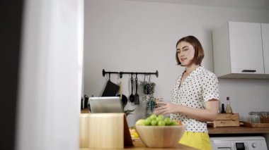 Kafkasyalı anne, modern mutfakta dizüstü bilgisayarda yemek tarifine bakarken salata yapmak için yemek hazırlıyor. Yetenekli ev bekçisi taze sebze kullanarak kahvaltı hazırlıyor. Pedagoji.