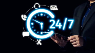 Modern bir işadamı neon 24 saatlik destek ikonunu gösteren bir tablet tutuyor ve günümüz dijital dünyasında sürekli müşteri hizmetleri ve iletişiminin önemini gösteriyor. Dörtgen