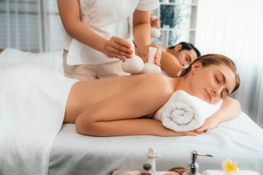Sıcak bitkisel top spa masaj vücut tedavisi, masör nazikçe bitki torbasını çift müşteri vücuduna bastırıyor. Aromaterapi dinlenme sükuneti ve sükuneti kaplıca salonundaki atmosferi aydınlatıyor. Sessiz.