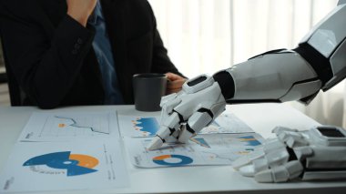 Robot bir kol, modern bir ofiste kahvesini yudumlarken iş haritalarını ve grafiklerini analiz eder. Bu resim teknoloji ve analizlerin kesişimini gösteriyor. Noogenesis