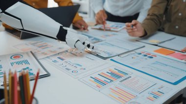 Çeşitli profesyonel bir ekip, veri analizi ve iş stratejisi gelişiminde verimliliği artırmak için robotik bir kol kullanarak ofis ortamında işbirliği yapmaktadır.