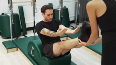 Erkek müşteri pilates ark fıçısında bacak kaldırma alıştırması yapıyor. Vücut dengesini, bacak dayanıklılığını ve spor salonundaki esnekliğini arttırmak için eğitmen yardımı ile birlikte. Öğrenci yalancı ve muziplik pozu veriyor. Alışkanlık.