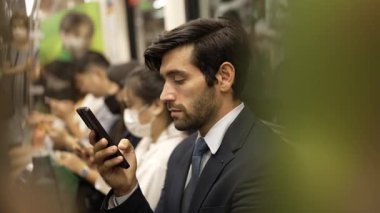 Gülümseyen beyaz iş adamı cep telefonuna bakıyor ya da trende otururken sosyal medya oynuyor. Çekici proje yöneticisi yoğun saatlerde toplu taşıma araçlarını kullanarak iş yerine gidiyor. Sevinçli..