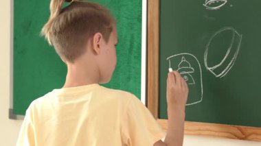 Kafkasyalı enerjik zeki çocuk sınıfta tahtada dururken hayal gücünü ifade etmek ve geliştirmek için resim çiziyor. Sanat dersinde karatahtaya yazı yazan çekici ilkokul öğrencisi. Pedagoji.