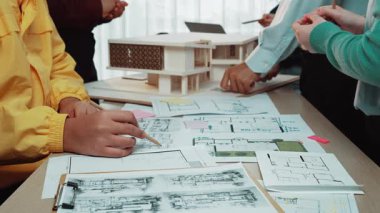 Canlı bir çalışma alanı gösteri ekibi üyeleri detaylı çizimler, renkli notlar ve işbirlikçi fikirlerle çevrili modern mimari planlarını tartışıyor, yaratıcılığı teşvik ediyor. SACTR