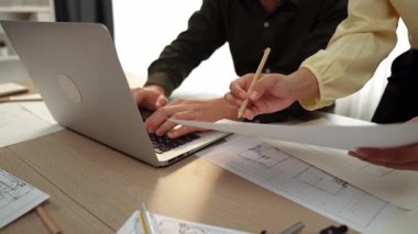 Architect and engineer compare construction detail blueprint display in laptop on table with architectural document or plan and measurement tool for accuracy at modern office. Closeup. Delineation.