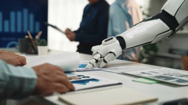 Bir robot kolu modern bir ofisteki belgelerle etkileşime geçerek, insanlar ve teknoloji arasındaki verimliliği ve yenilikçi iş akışını geliştirmek için kusursuz işbirliğini gösteriyor.