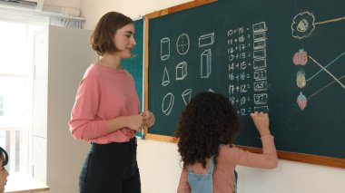 İlkokulda Afrikalı bir kızın tahtaya cevap yazmasına bakan yetenekli beyaz bir öğretmen. İlkokul sınavına cevap vermek için sınıfın önünde yürüyen profesyonel bir öğrenci. Pedagoji.