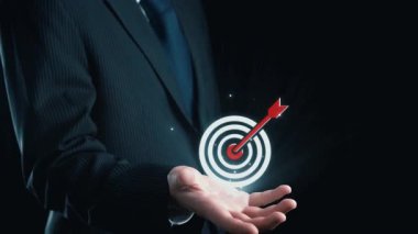 Bir işadamı, analitik ve iş stratejilerinin dijital simgeleri ile çevriliyken hedeflere ve başarıya odaklanmayı sembolize eden bir ok ile hedef grafiğini sergiliyor. Dörtgen