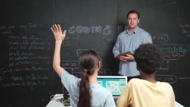 Kodlama programıyla ilgili öğrenci sorusuna beyaz öğretmen cevap veriyor. Beyaz kız, STEM teknoloji sınıfında dizüstü bilgisayar ekranı görüntülerken soru sormak, oy vermek, gönüllü olmak için elini kaldırdı. Öğretim
