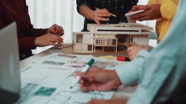 Mimarlar modern bir ofiste proje tasarımlarını incelerken işbirliği yapıyorlar, ayrıntılı çizimler ve modeller masaya yayılarak yaratıcılık ve takım çalışması sergiliyorlar. SACTR