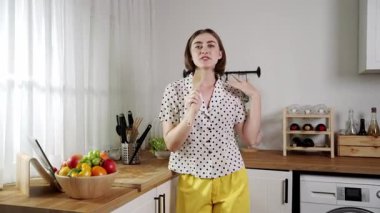 Enerjik beyaz anne kahvaltı için salata pişirirken ve yemek pişirirken elinde kepçeyle şarkı söylüyor. Sağlıklı yemek yapmaya hazırlanırken müziğe yönelen mutlu ev sahibi. Pedagoji.