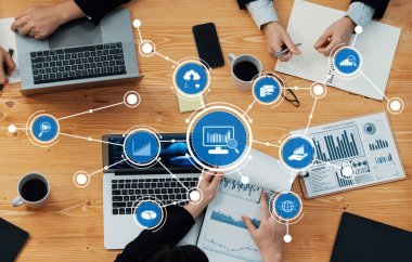 Bir konferans masası etrafında birden fazla dizüstü bilgisayar, veri analizi görselleri ve takım çalışmasının yer aldığı, işbirlikçi stratejiler ve sezgilerin geliştirildiği profesyonel bir iş toplantısı. Dostluk