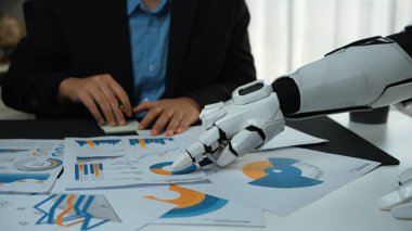Bir insansı robot renkli grafiklerle finansal belgelere odaklanırken bir yandan da iş dünyasının profesyonel jestlerine odaklanıyor. Bu sahne şirket analizlerinde yenilikleri yakalar. Noogenesis
