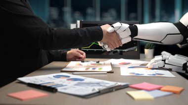 Bir insan ve robotik kol modern ofis ortamında teknoloji ve iş arasındaki işbirliğini sembolize eden bir tokalaşmaya girişirler.