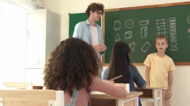 Profesyonel öğretmen konuşuyor ve sınıfta Asyalı çocuğa fikrini açıklıyor. Sınıfın önünde karatahta matematik dersiyle dikilmiş beyaz öğrenci dinleme eğitmeni. Pedagoji.