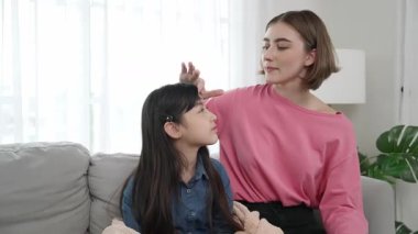 Kafkasyalı anne kızını kucaklıyor ve kanepede oturuyor ve alnından öpüyor. Mutlu anne oturma odasında sevimli Asyalı liseli kıza sevgi ve sevgi gösteriyor. Güzel bir aile birlikte vakit geçirir. Pedagoji.