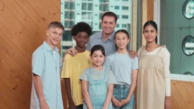 Mutlu öğretmen ve çeşitli öğrenciler kameraya gülümserken ayakta duruyorlar. Profesyonel akıllı eğitmen ve karışık ırk olan lise öğrencileri kameraya neşeli pozlar veriyor. Öğretim