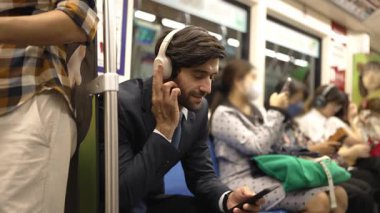 Gülümseyen yakışıklı yatırımcı trende otururken rahatlatıcı müzik dinliyor. Profesyonel iş adamı iş yerine toplu taşıma araçlarıyla giderken müzik dinlemeyi sever. Arka plan bulanık. Sevinçli..