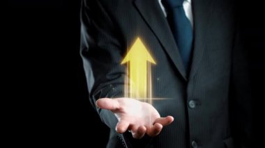 Takım elbiseli bir işadamı elini yukarı doğru parlayan bir ok grafiğiyle uzatarak, finansal büyüme ve modern iş stratejileri ve yatırımlarındaki başarıyı sembolize ediyor. Dörtgen